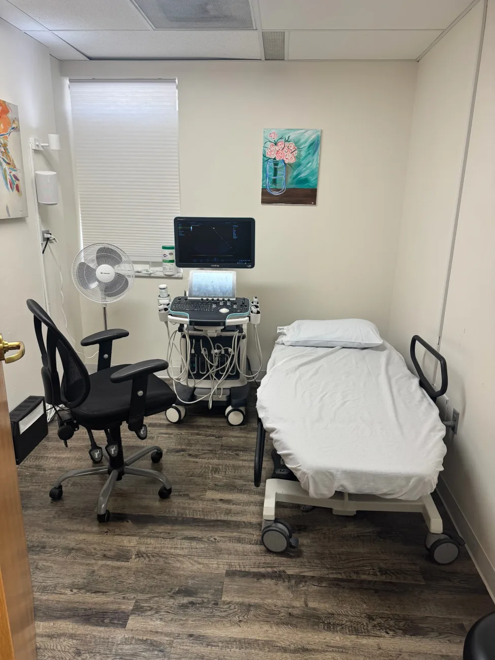 An exam room with a made table, floral artwork, and an ultrasound system