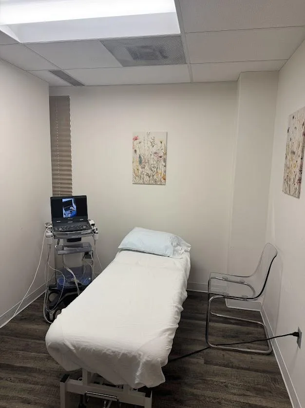 An exam room with window light, wildflower artwork, and an ultrasound cart